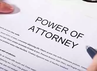 A person is holding and signing a document titled "Power of Attorney.