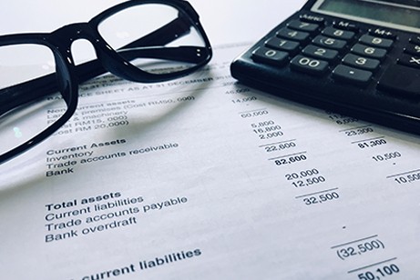 A pair of glasses and a calculator rest on top of a financial statement listing assets and liabilities.