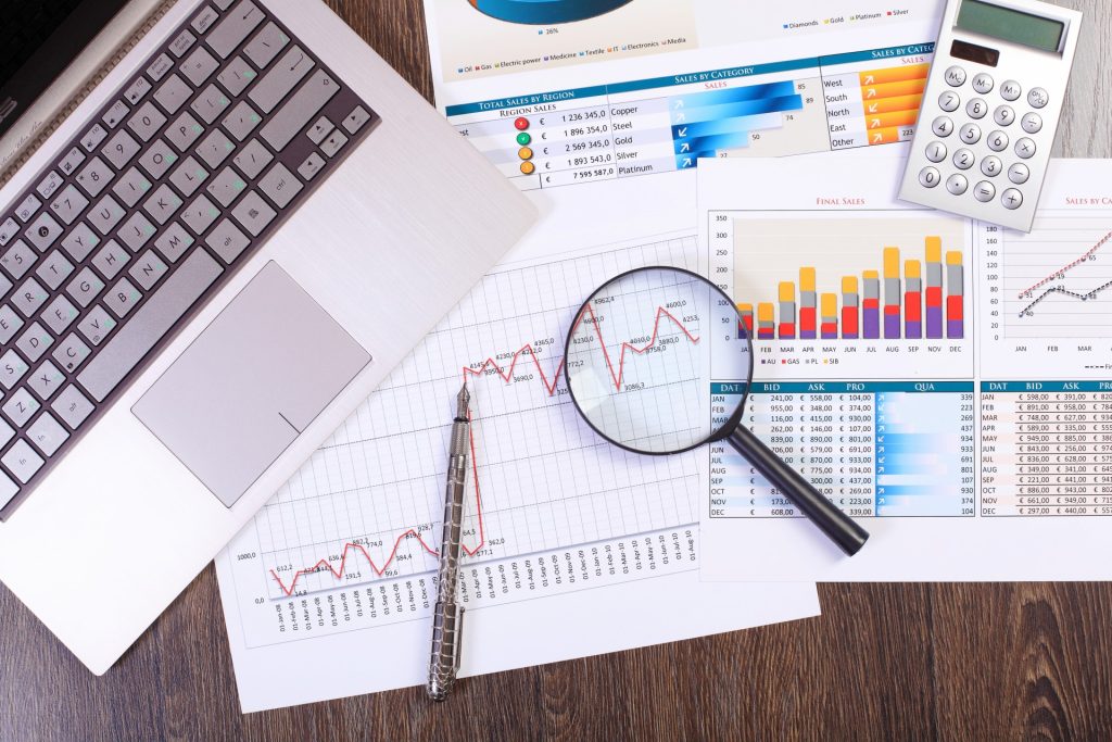Laptop, pen, magnifying glass, and calculator on a desk with printed charts and graphs displaying financial and sales data analysis—ideal tools for a Chandler Estate Planning Attorney reviewing client portfolios.