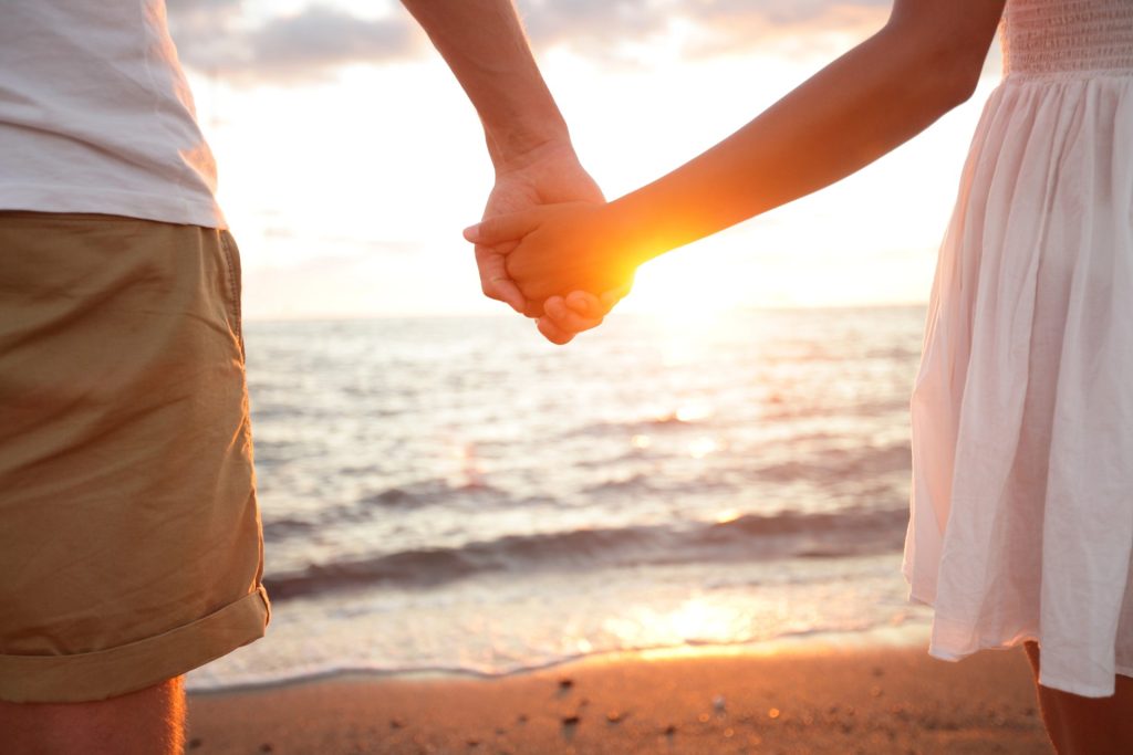 Two people holding hands while standing on a beach at sunset, with sunlight shining between them—just as a Mesa Estate Planning Attorney helps you safeguard your future with clarity and peace of mind.