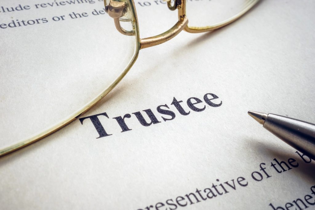 Close-up of the word "Trustee" printed on a document, with part of a pair of eyeglasses and a pen visible nearby—an image often seen in the office of a Mesa Probate Attorney.