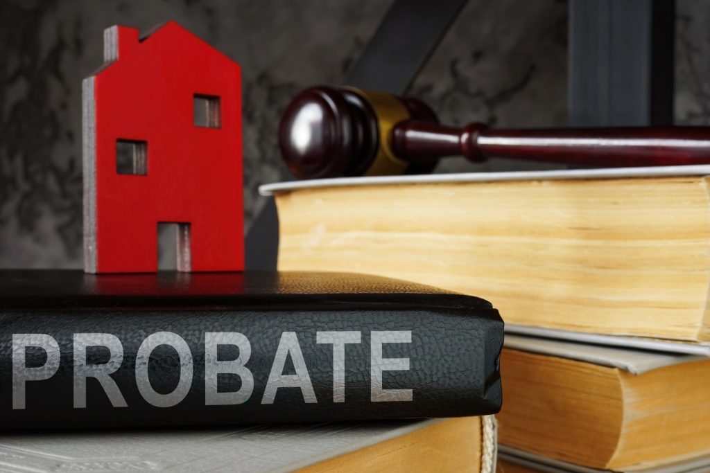 A book labeled "PROBATE," a small red house figurine, a judge's gavel, and two thick legal books are arranged together on a table, symbolizing the guidance of a skilled Mesa Probate Attorney.