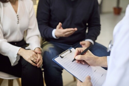 Doctor and couple reviewing clipboard notes during medical consultation meeting